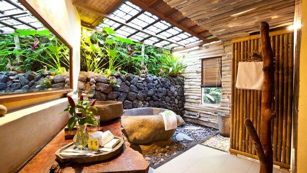 Un espacio de spa con pared de piedra, una bañera de madera y un banco de madera.