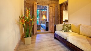 Un pasillo con una puerta de madera que da a un dormitorio, un sofá con cojines y una planta en maceta con flores rojas.
