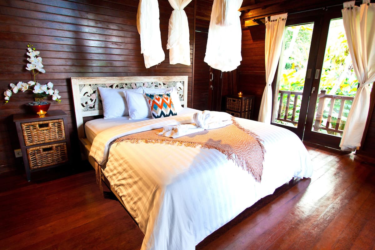 A wooden-paneled bedroom with a large bed, a nightstand with a lamp, and a window with curtains.