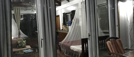 A room with a bed, a chair, and a sliding glass door leading to another room.