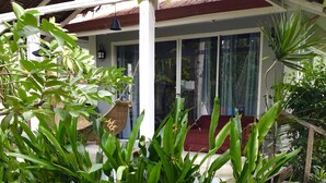 A covered porch with a red cushioned seating area, surrounded by lush green plants. - Siargao Residency (General Luna)