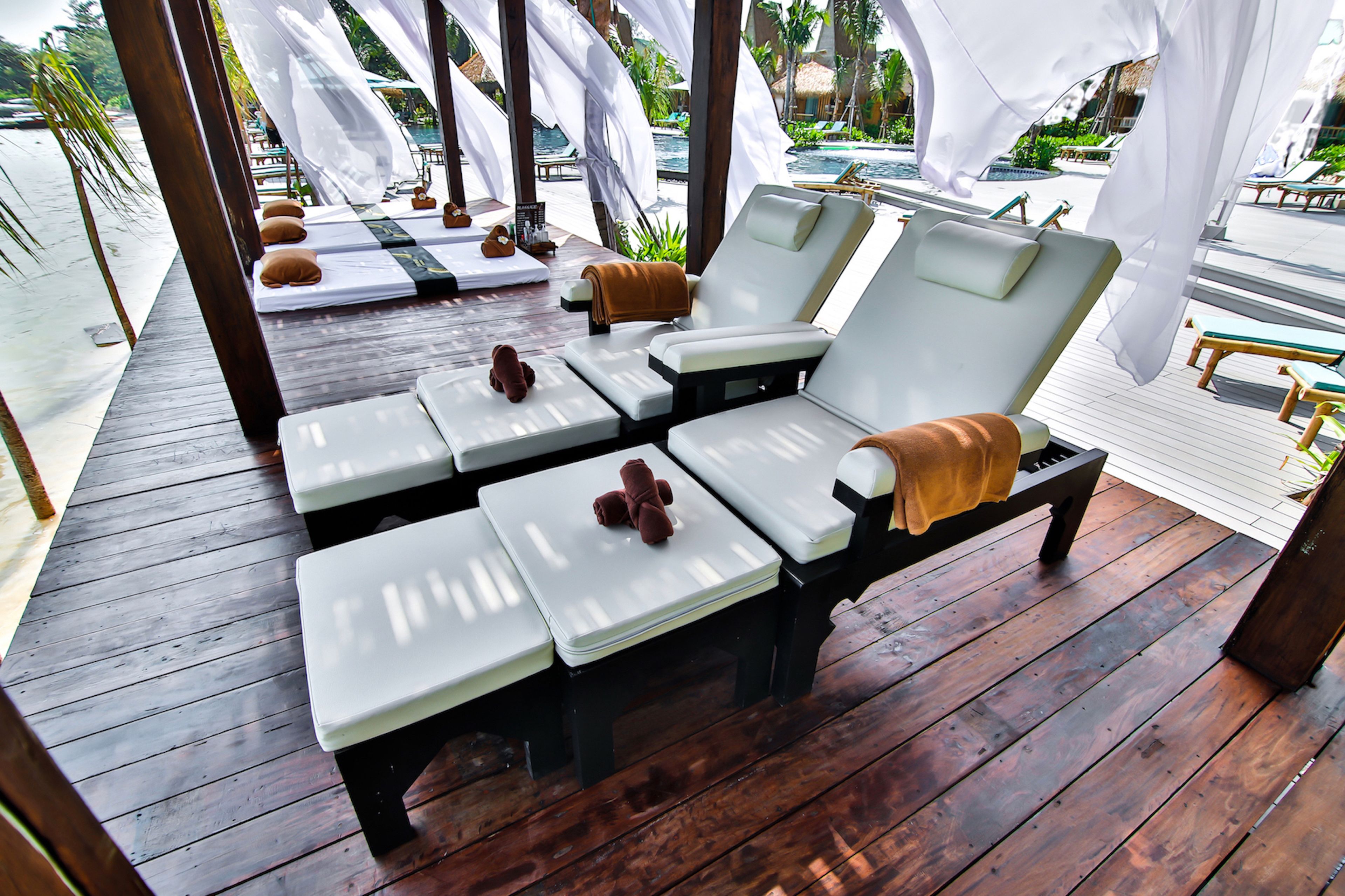 Une terrasse en bois avec des chaises longues et des serviettes, donnant sur un espace piscine.