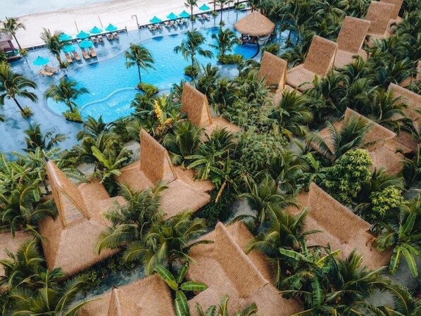 Een resort met meerdere zwembaden, omgeven door palmbomen en bungalows met rieten daken.