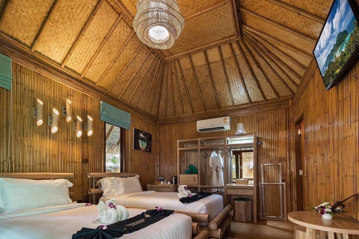 Een kamer ingericht in bamboestijl met twee bedden, een televisie en een tafeltje.