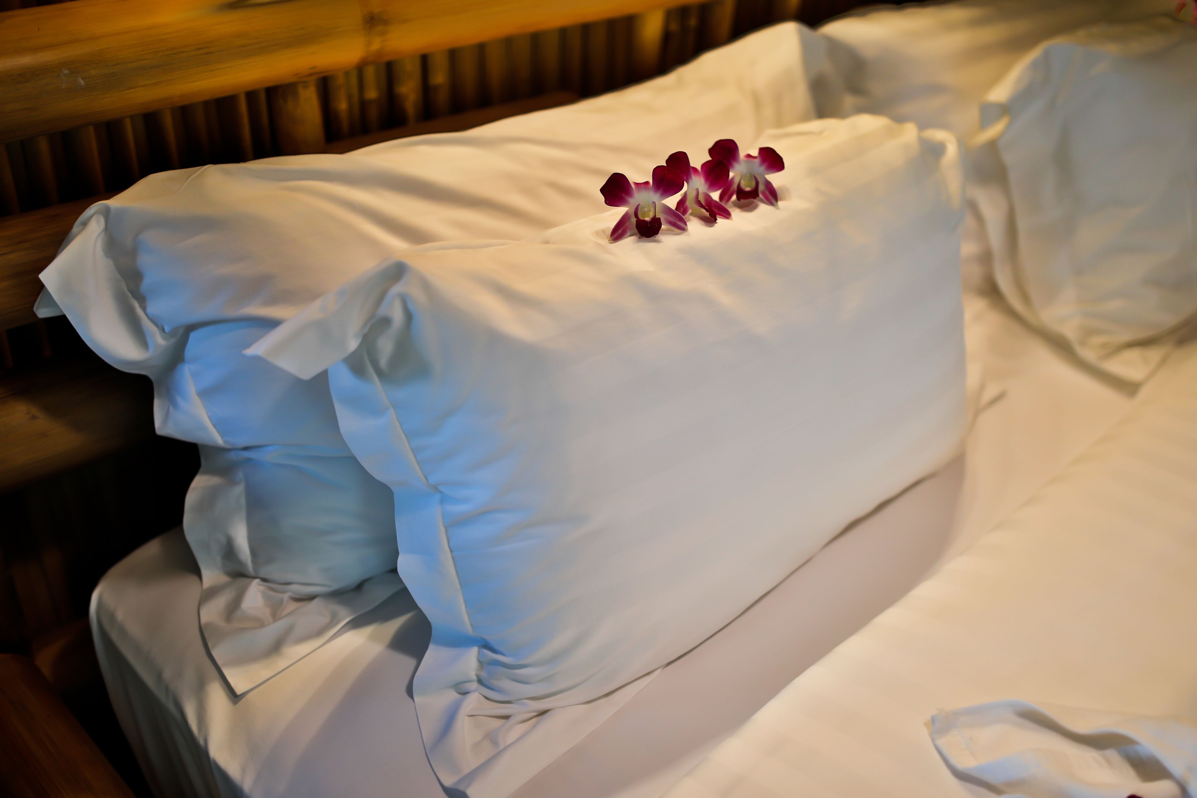 A neatly made bed with white linens and a decorative arrangement of purple and white flowers on the pillow.