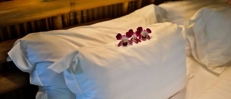 A neatly made bed with white linens and a decorative arrangement of purple and white flowers on the pillow.