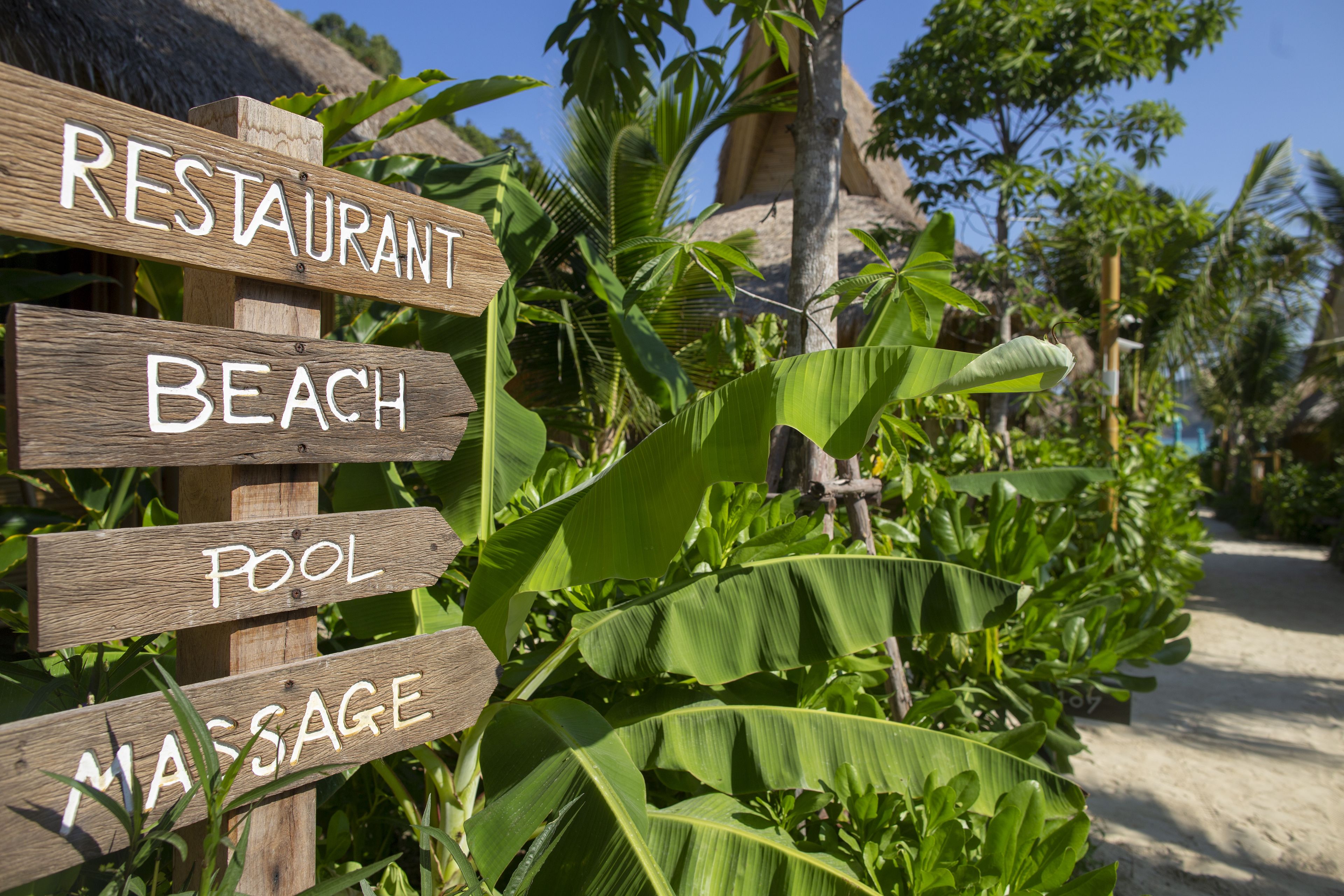 A wooden sign with the words "RESTAURANT," "BEACH," "POOL," and "MASSAGE" indicating nearby amenities.