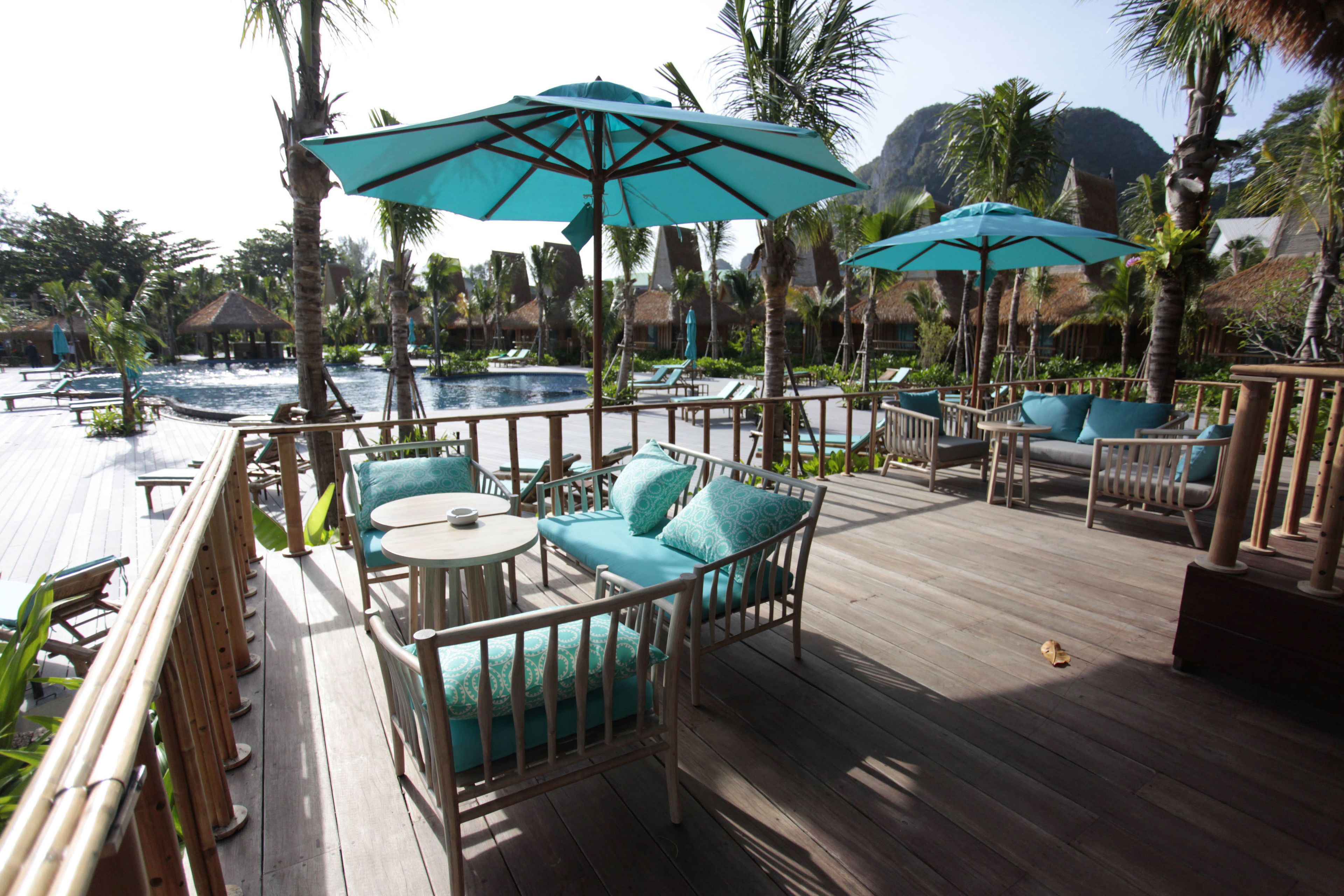 Une terrasse en bois avec des meubles d’extérieur, notamment des chaises et un canapé, située près d’une piscine.