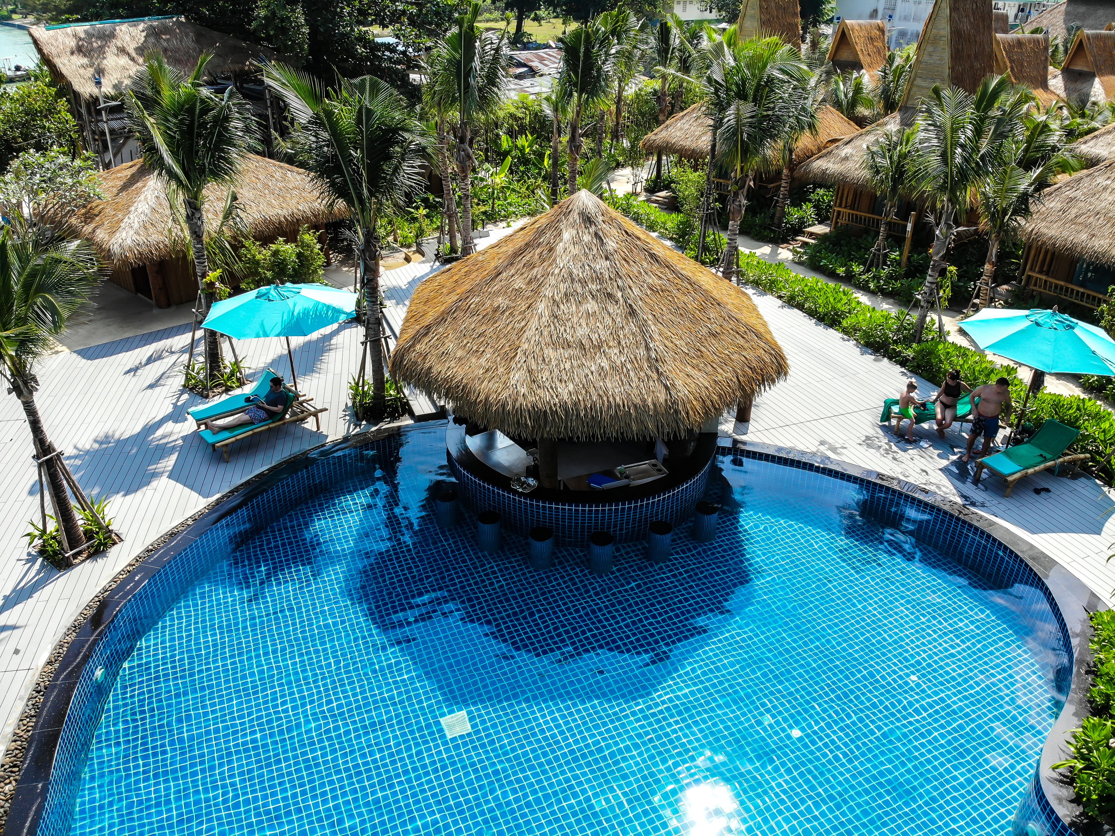 Una piscina con una estructura de techo de paja en el centro, rodeada de sillones de playa y sombrillas.