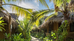 Un sentier qui traverse un complexe hôtelier tropical, avec des huttes aux toits de chaume et une végétation luxuriante.