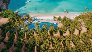 Un complexe hôtelier doté d’une piscine entourée de palmiers et d’une plage aménagée avec des parasols.