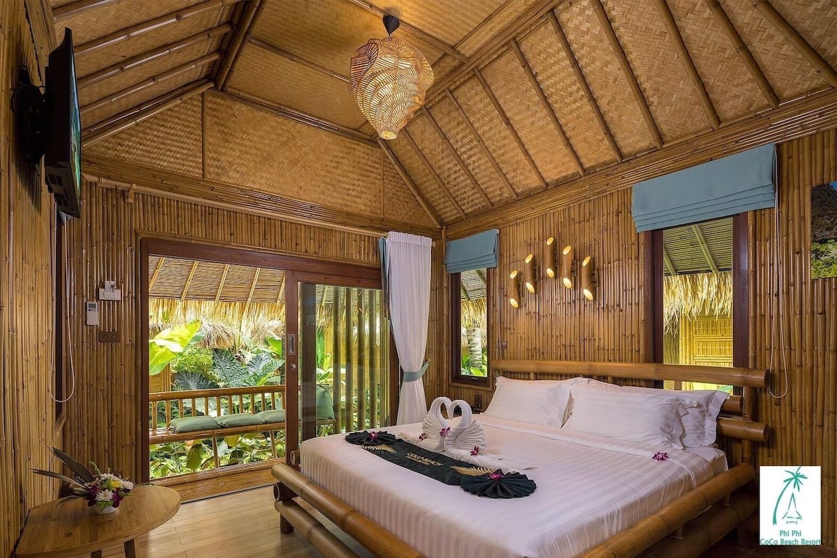 Een kamer met bamboe decoratie, een bed, een televisie en uitzicht op groen.