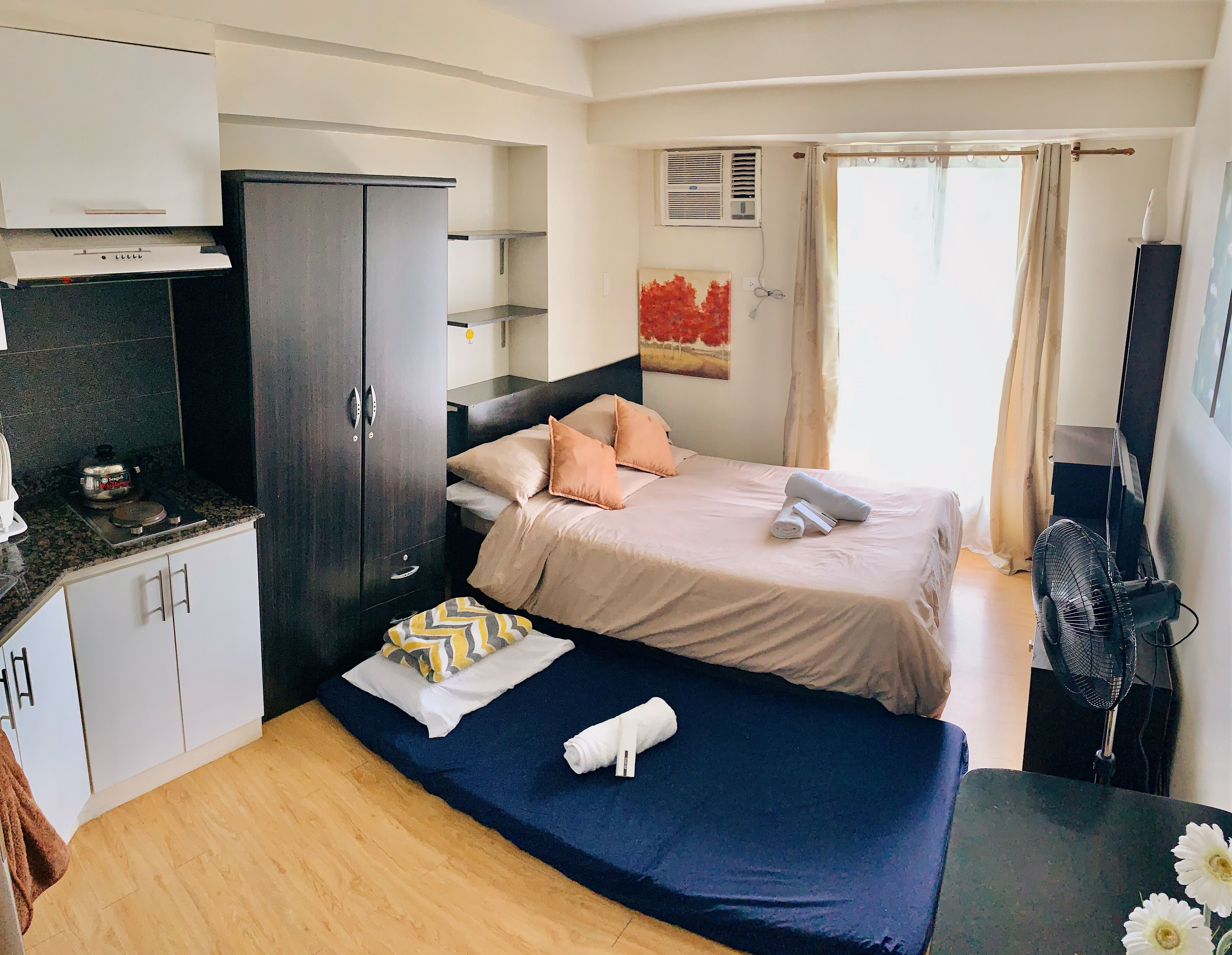 Una habitación de hotel compacta con una cama, una kitchenette pequeña, un escritorio y un televisor.