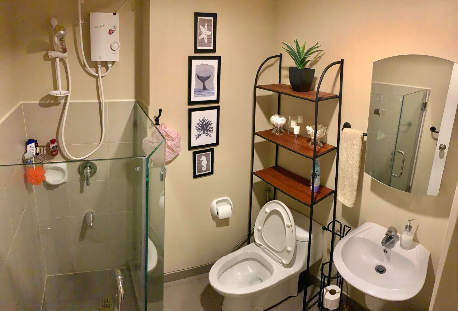A compact bathroom with a glass shower enclosure, a toilet, a sink, and a shelf unit with decorative items.