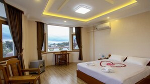 A hotel room with a large bed, a desk, and a view of the city. - Five One Star Hotel (Nyaungshwe)