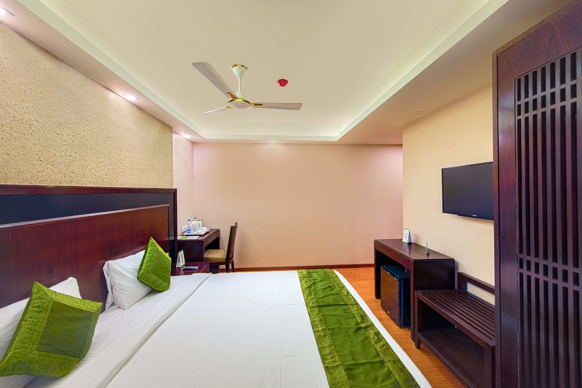 A hotel room with a bed, a desk, a chair, a television, and a ceiling fan.