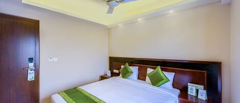 A hotel room with a bed, a nightstand, a wall-mounted clock, a ceiling fan, and a door with a digital lock.