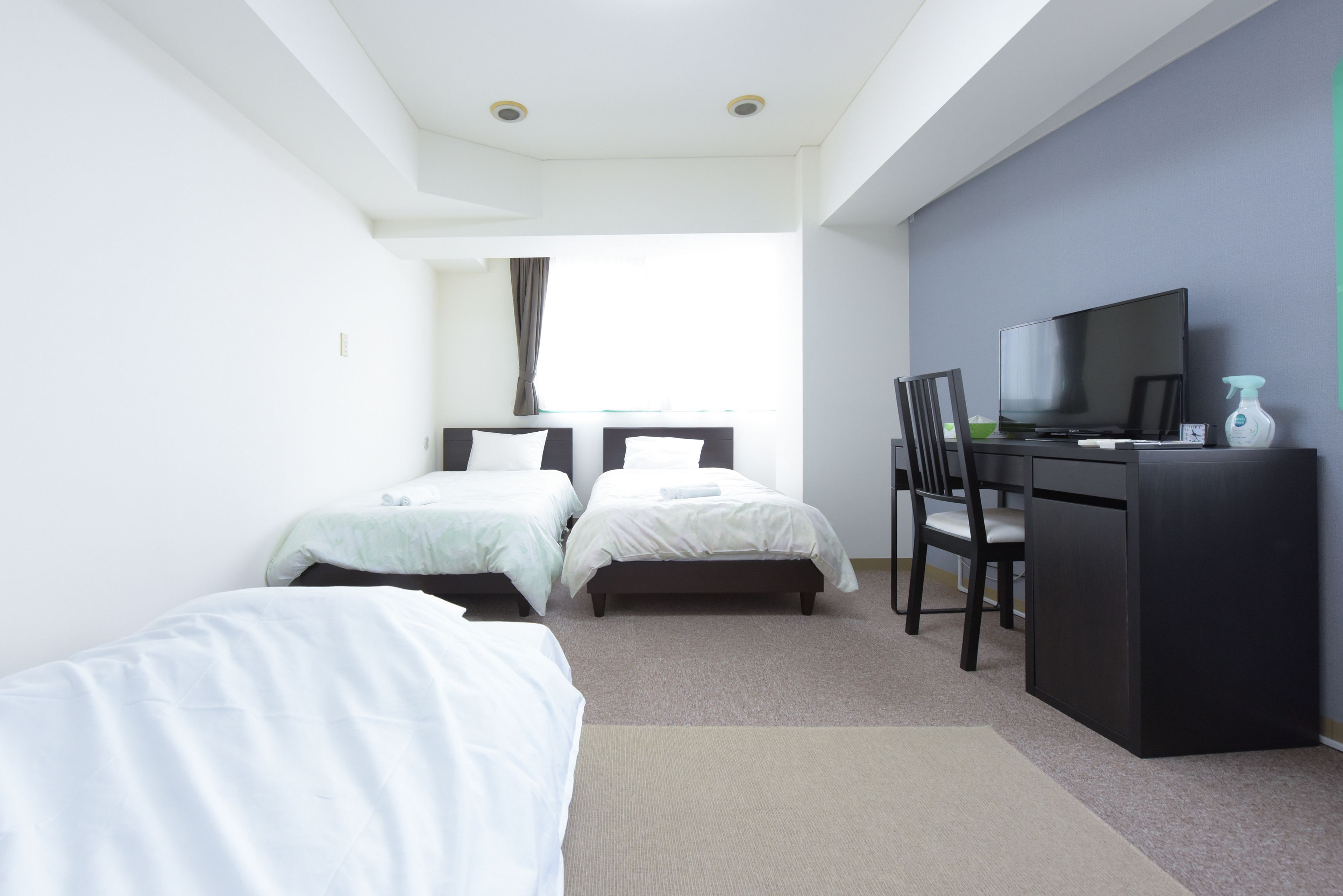 A hotel room with two beds, a desk with a TV, and a window with curtains.