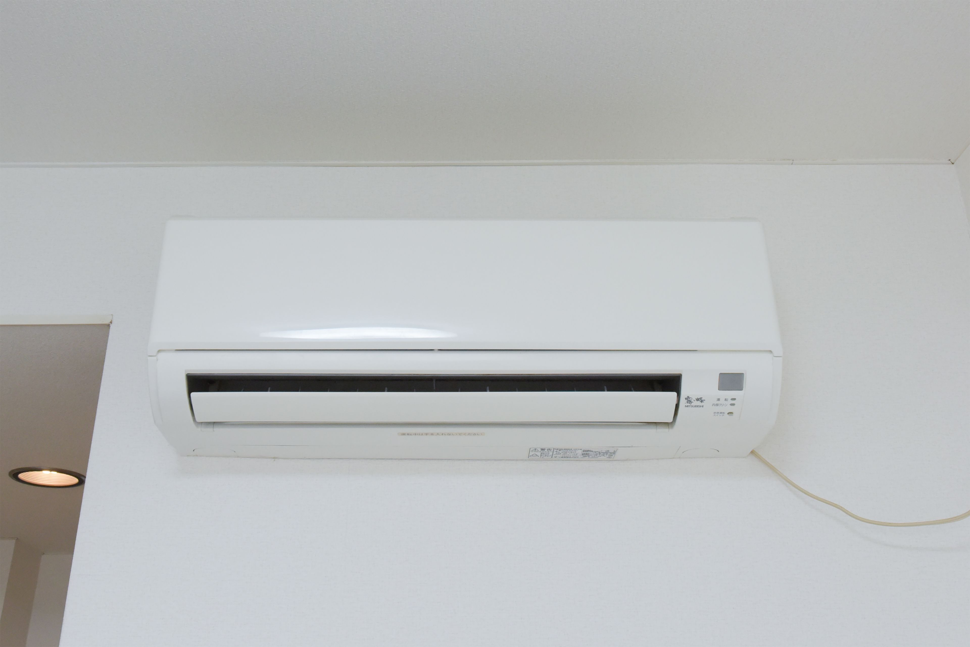 A white wall-mounted air conditioning unit with a control panel and a visible power cord.