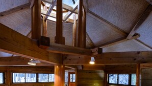 Interior de una cabaña de madera con techos altos, vigas de madera y una pared con ventanales.