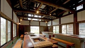 Un interior rústico con bancos y mesas de madera, ventanas amplias y un techo alto con vigas a la vista.