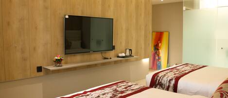 A hotel room with a wooden panel wall, a mounted flat-screen TV, a shelf with a coffee maker, and two beds with patterned bedspreads.