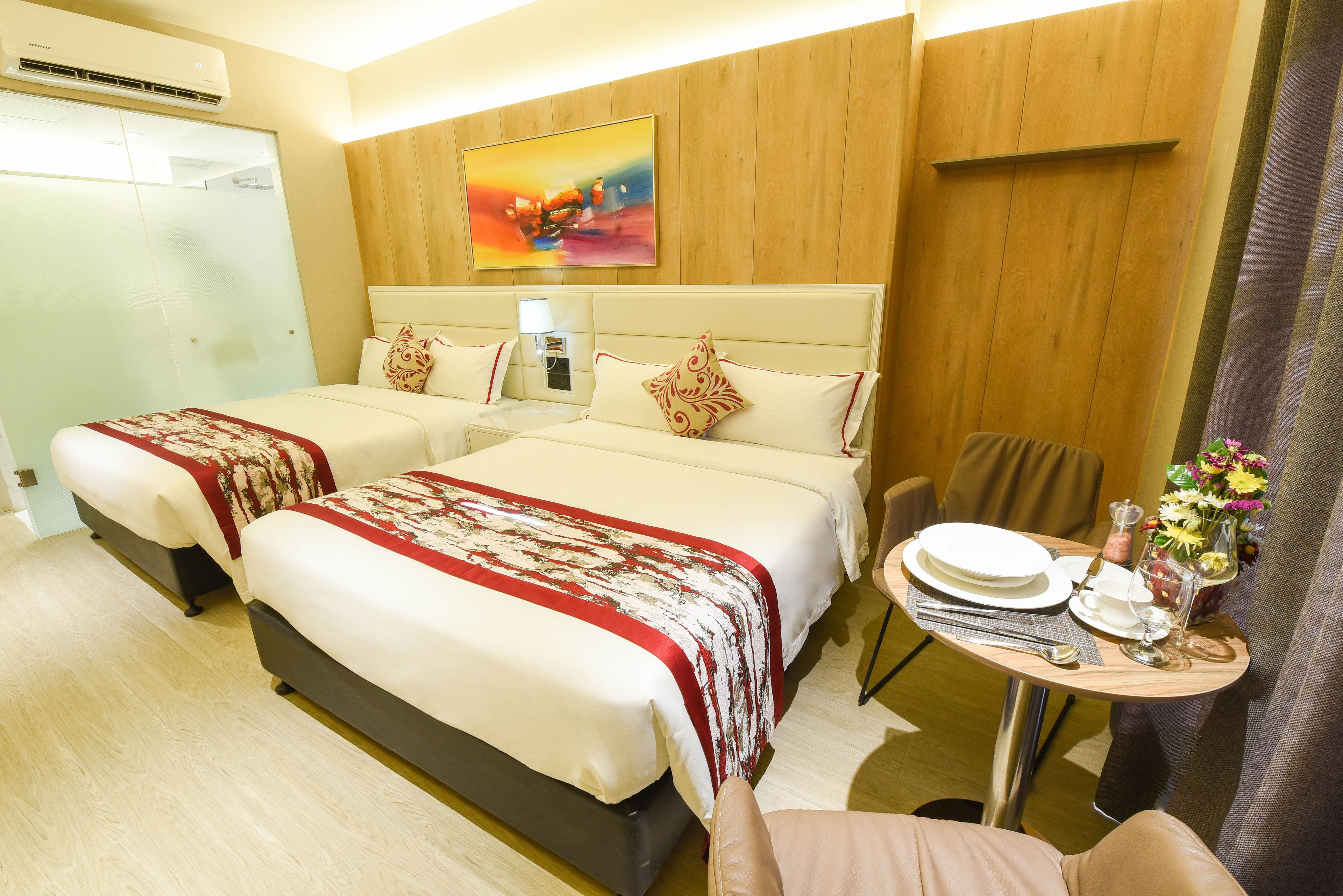 Habitación de hotel con dos camas, una mesa de comedor dispuesta con platos y vasos, y un cuadro en la pared.