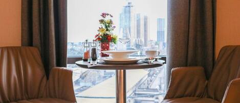A room with two leather chairs, a table with a vase of flowers, a cup, and a glass. A cityscape is visible through the window.
