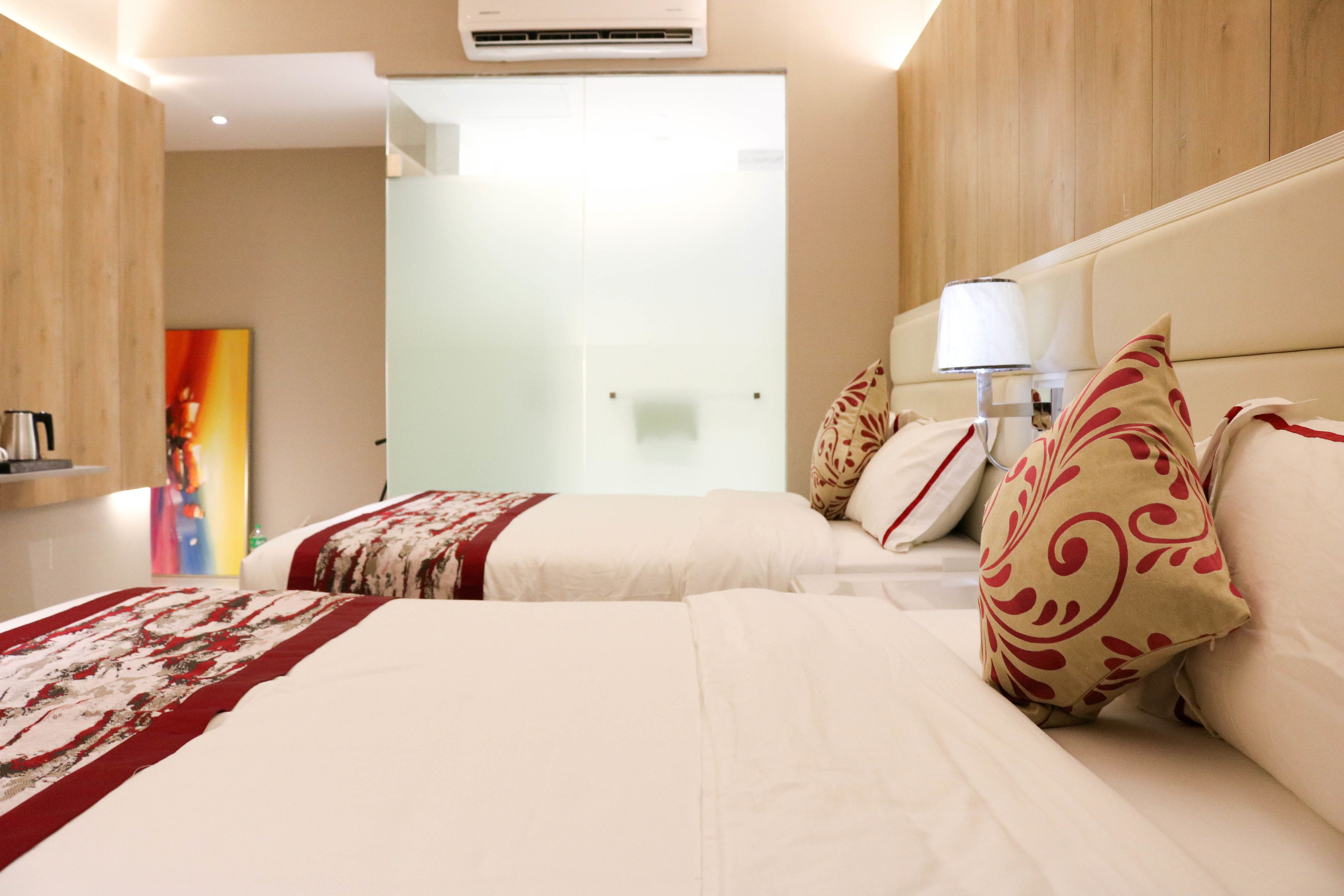 A hotel room with two beds, a wooden headboard, a bedside lamp, and a colorful painting on the wall.