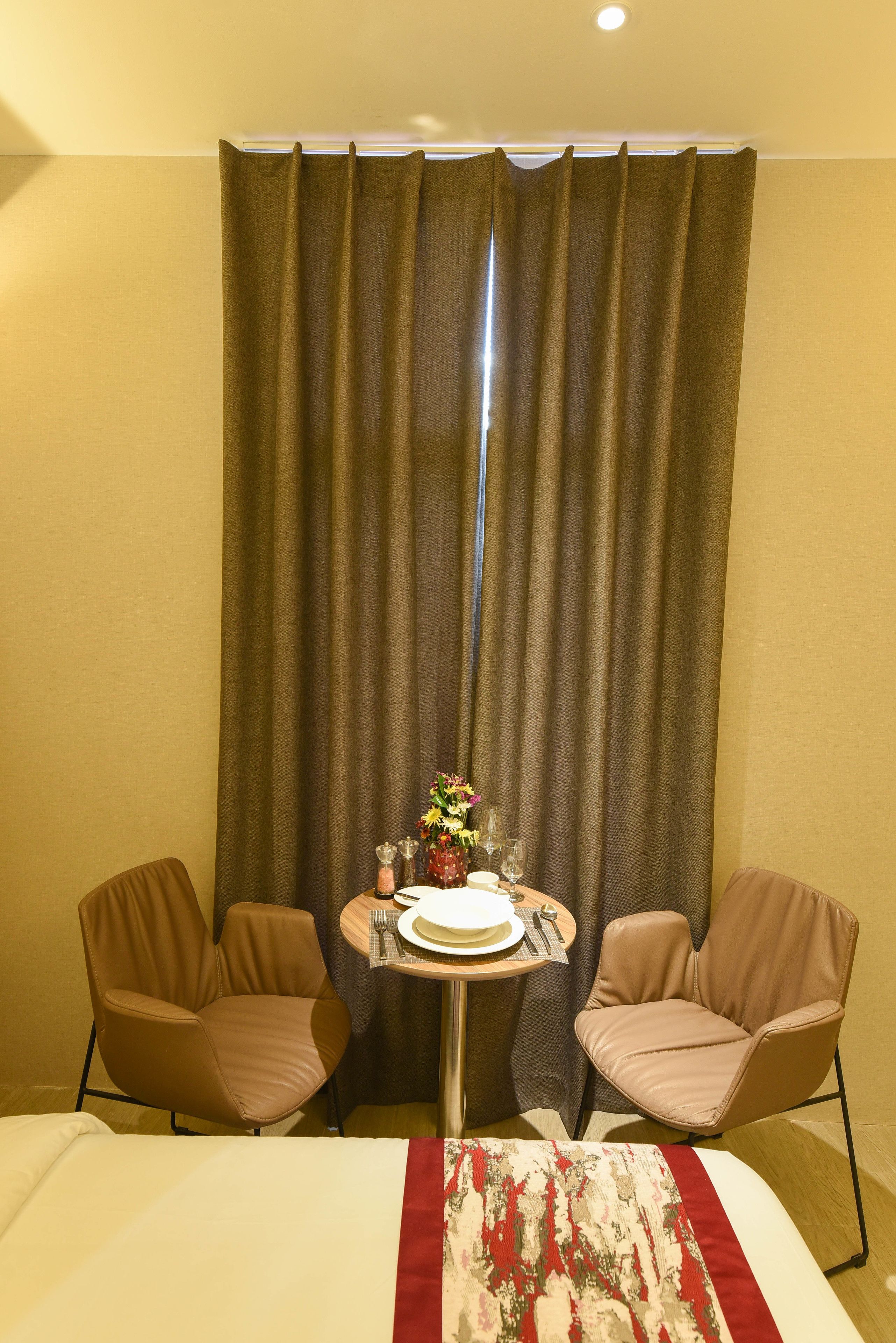 A hotel room with a bed, two chairs, a small table with a vase of flowers, and a curtain.