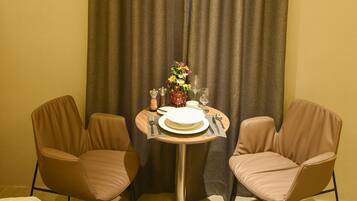 A hotel room with a bed, two chairs, a small table with a vase of flowers, and a curtain.