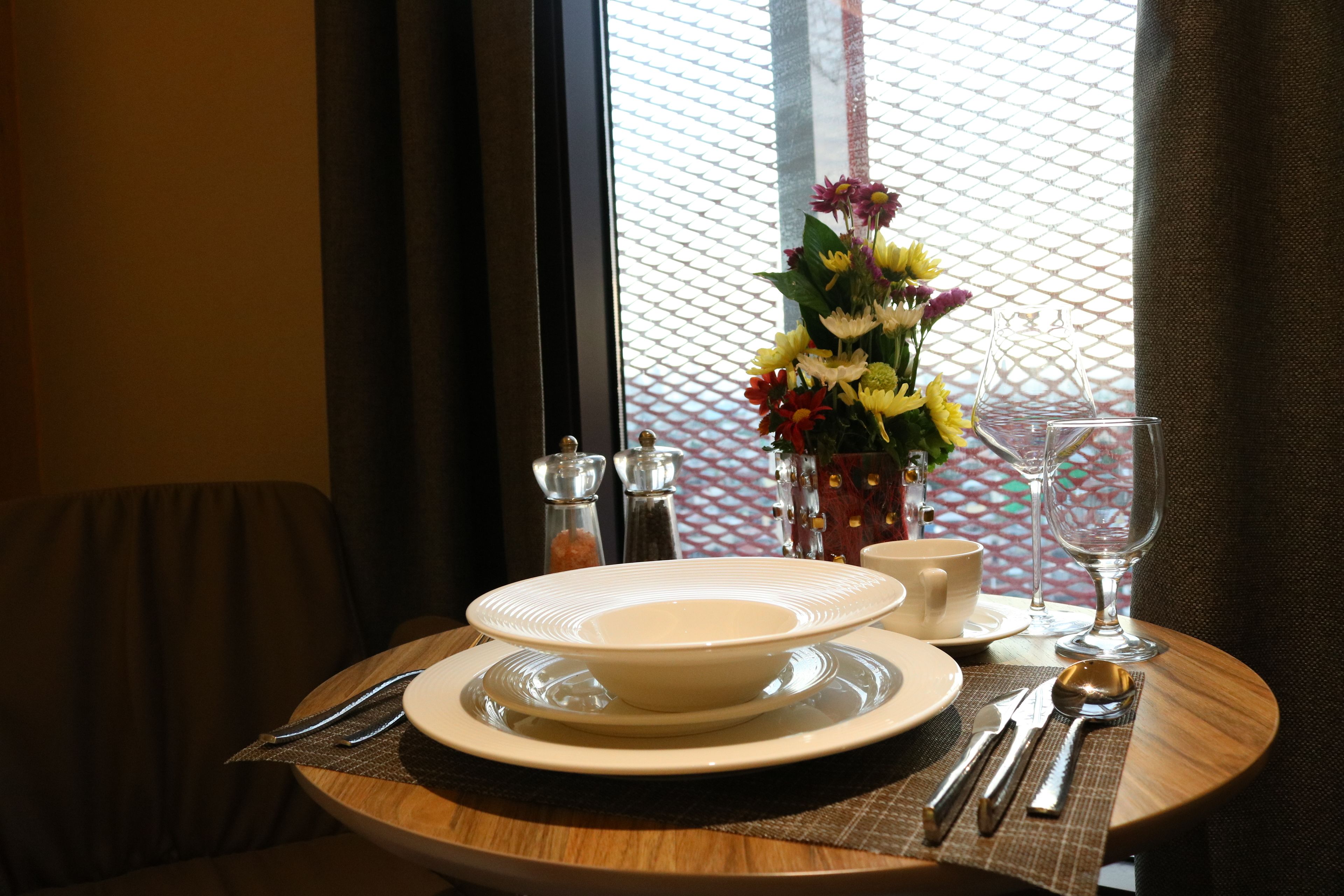 A dining table set with plates, cutlery, a glass, and a vase of flowers.