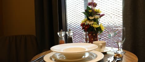 A dining table set with plates, cutlery, a glass, and a vase of flowers.