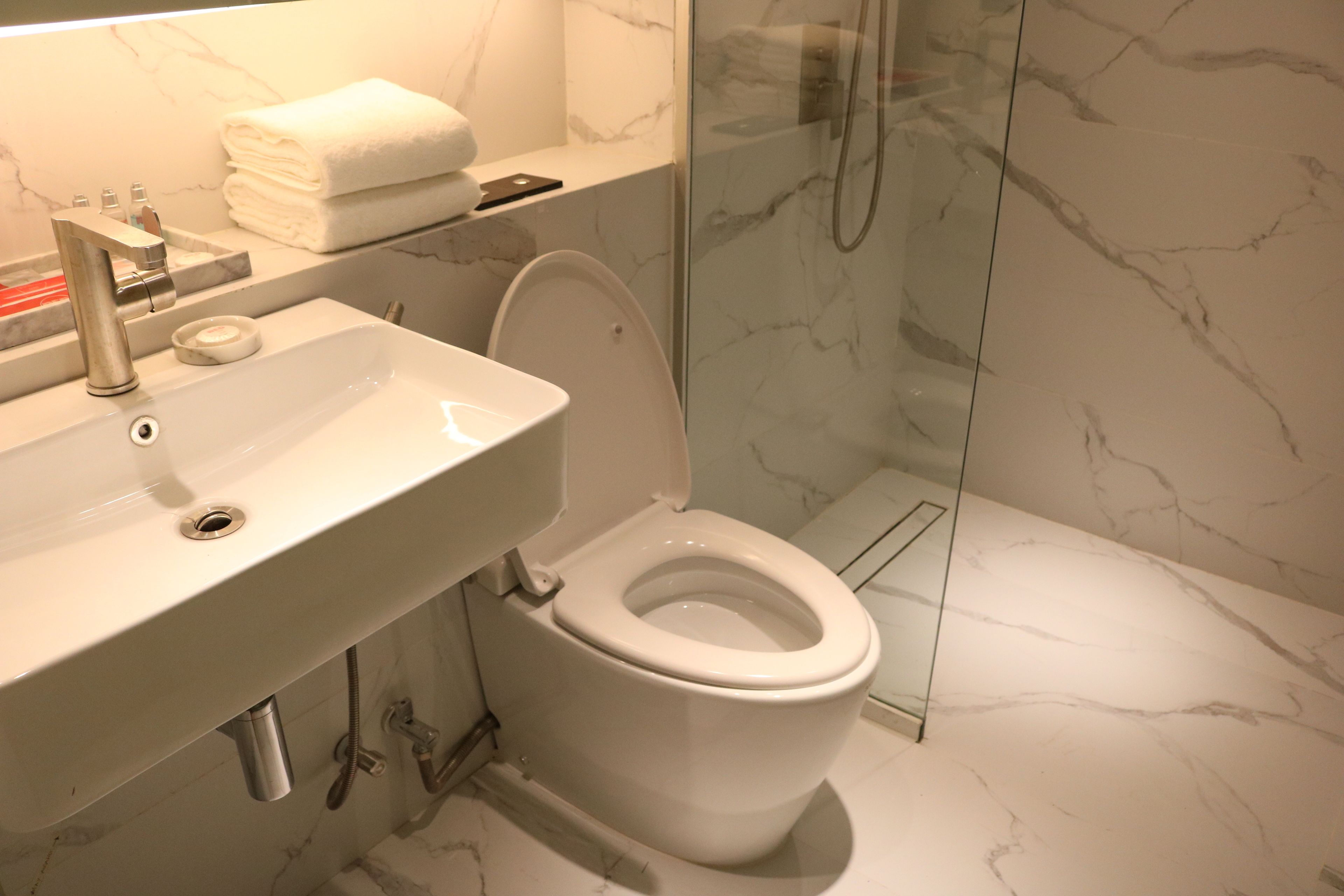Un baño moderno con lavamanos blanco, inodoro y ducha con mampara de vidrio.