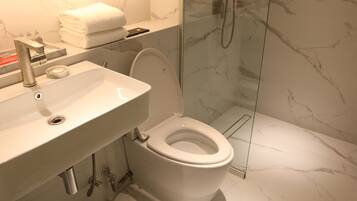 Un baño moderno con lavamanos blanco, inodoro y ducha con mampara de vidrio.