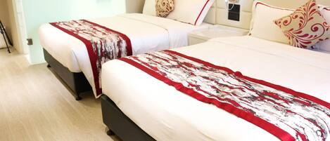 A hotel room with two beds, each with a red and white patterned bedspread, a wooden headboard, and a bedside table with a lamp.