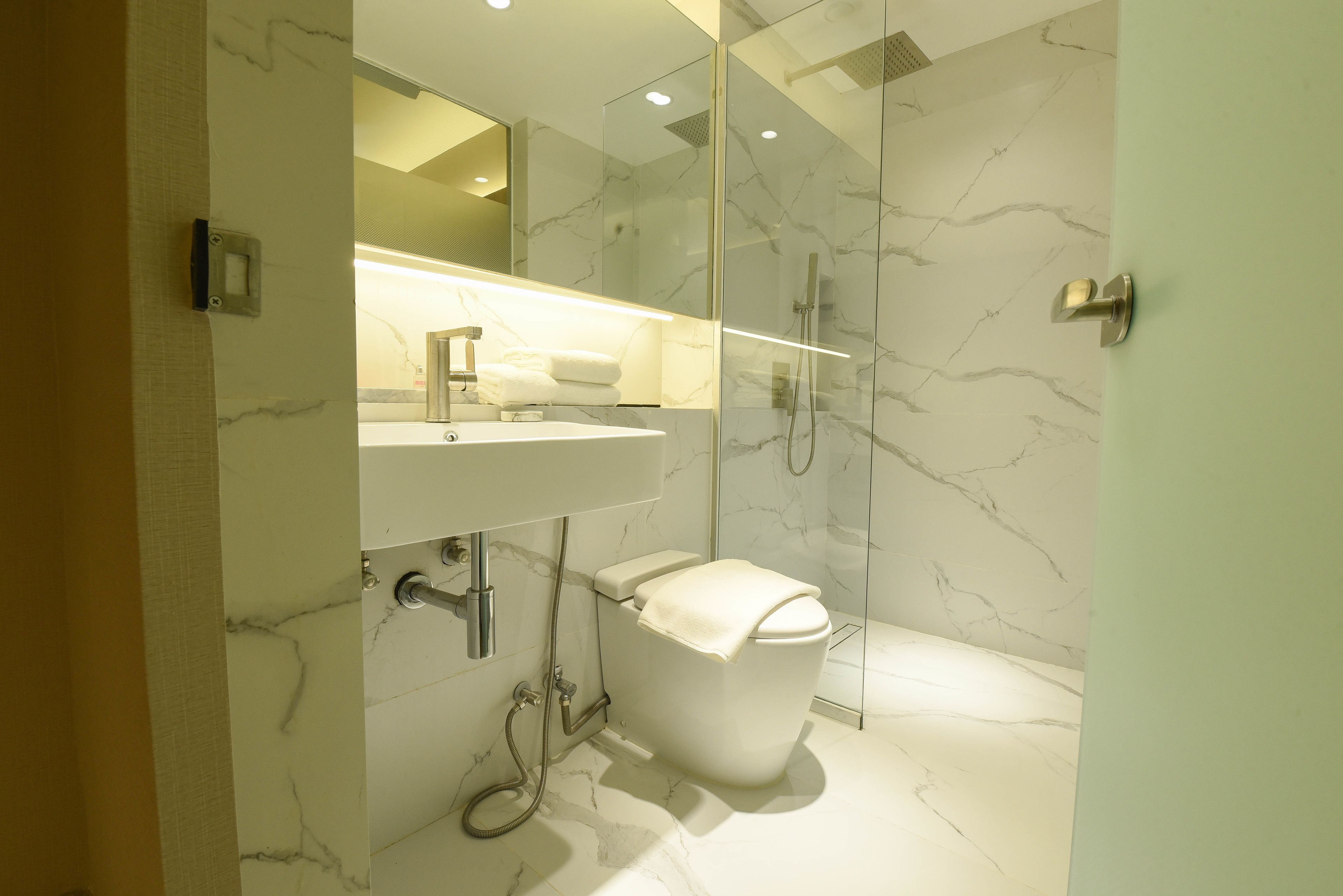 A modern bathroom with a marble floor, a white toilet, a glass-enclosed shower, and a vanity with a mirror.