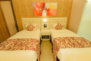 Habitación de hotel con dos camas, cada una con cabecero, mesita de noche con lámpara y una obra de arte colgada en la pared sobre las camas.