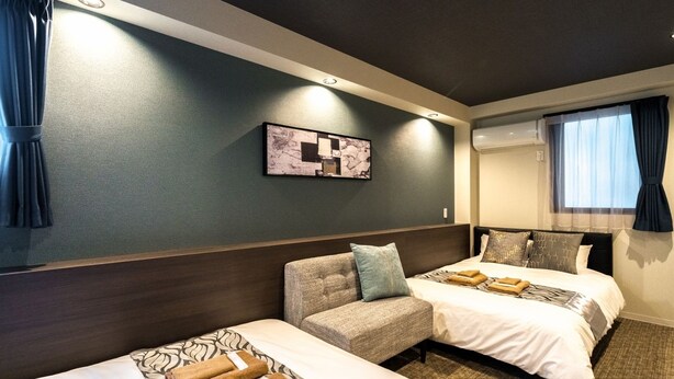 A hotel room with two beds, a sofa, a wall-mounted artwork, and a window with curtains. - UCHI Asakusabashi (Tokyo)