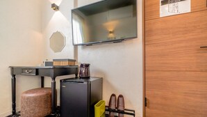 A hotel room with a desk, a small refrigerator, a coffee maker, a shoe rack, and a television mounted on the wall. - UCHI Asakusabashi (Tokyo)