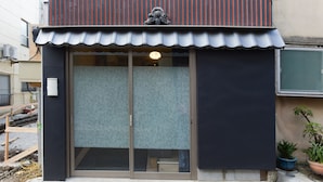 Un edificio con tetto in metallo, ingresso con vetrata scorrevole e una piccola tenda da sole.