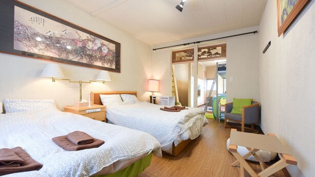 Una camera d'albergo con due letti, una scrivania e una sedia. C'è un quadro appeso al muro e una porta scorrevole che conduce a un'altra stanza.