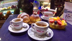 Una mesa con dos tazas de café, un croissant, un pastel y un cuenco con fruta.