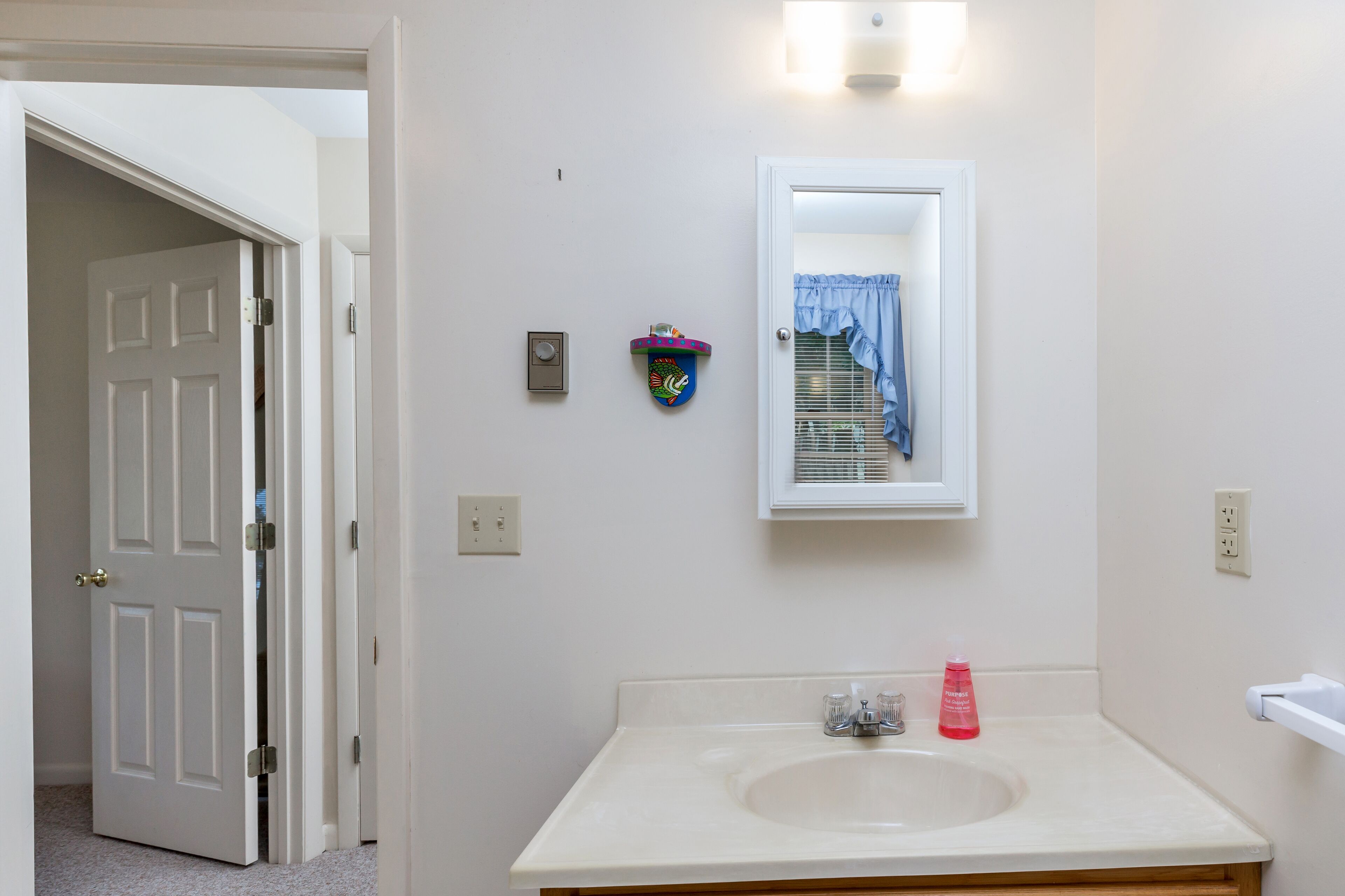 Une salle de bain avec un lavabo blanc, un miroir et une porte donnant sur une autre pièce.
