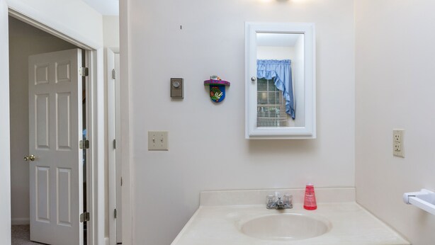 A bathroom with a white sink, a mirror, and a door leading to another room. - Beach Pines by Seaside Vacations & Sales (Chincoteague Island)