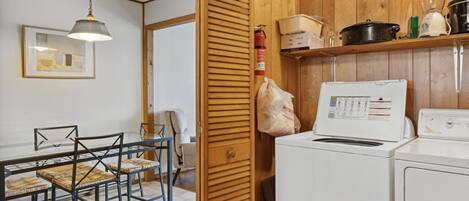 A compact kitchen with wooden cabinets, a washing machine, and a dining area with chairs and a table.