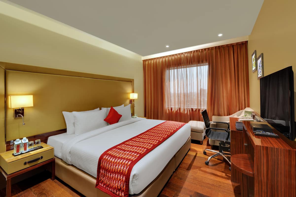 Une chambre d’h ôtel avec un grand lit, un bureau, une chaise, une télévision et une fenêtre avec des rideaux.