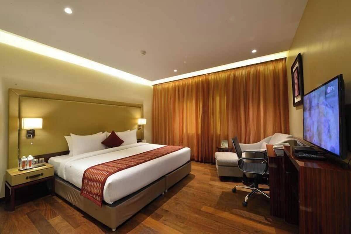 Une chambre d’hôtel comprenant un lit, des tables de chevet, un bureau, une chaise, un téléviseur et un rideau.