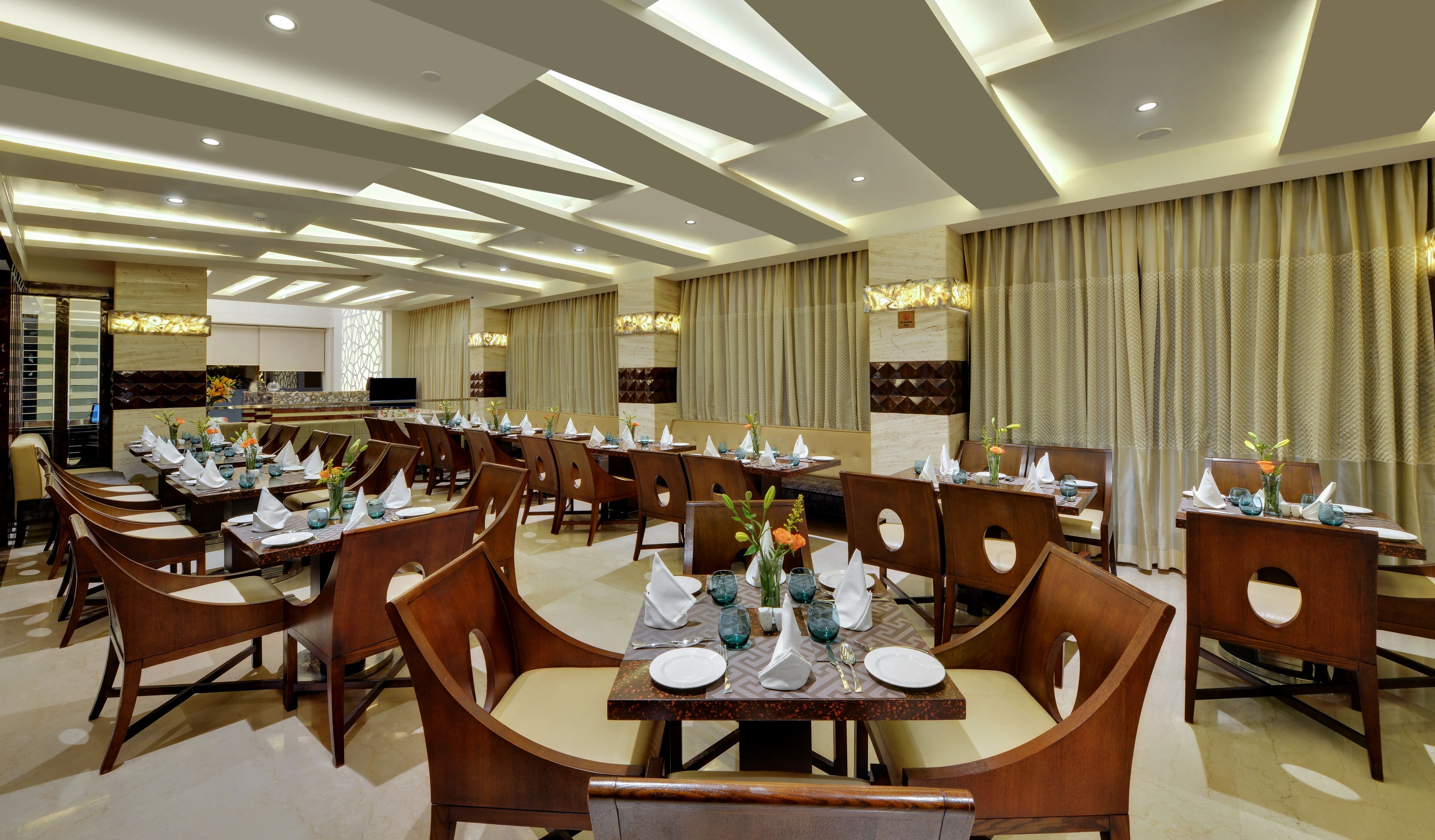Un vaste espace dédié à la salle à manger, avec de nombreuses tables dressées, des chaises en bois et un design moderne au niveau du plafond.