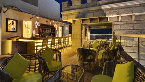 Un bar situé sur le toit, avec des chaises en osier et un espace bar comprenant un comptoir et des sièges.